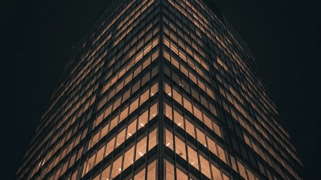 Looking up the corner of a glass office tower at night, floors lit from within